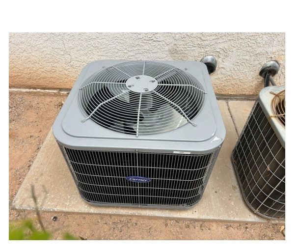 Outdoor air conditioning unit placed on a concrete slab near a beige wall.