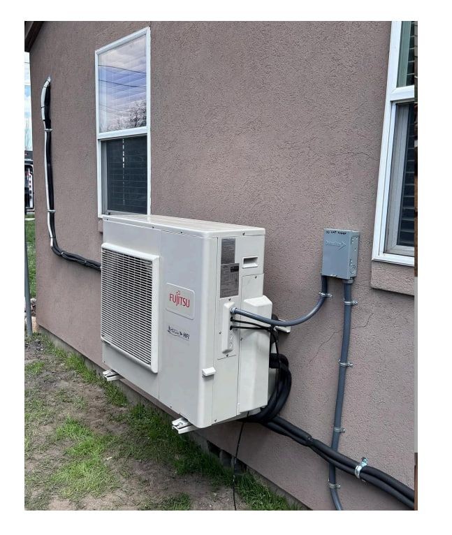 Exterior wall-mounted Fujitsu air conditioning unit installed outside a residential building with electrical wiring connected.