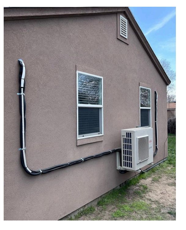 Exterior wall of a house with air conditioning unit installed, connected to ducts running along the side.