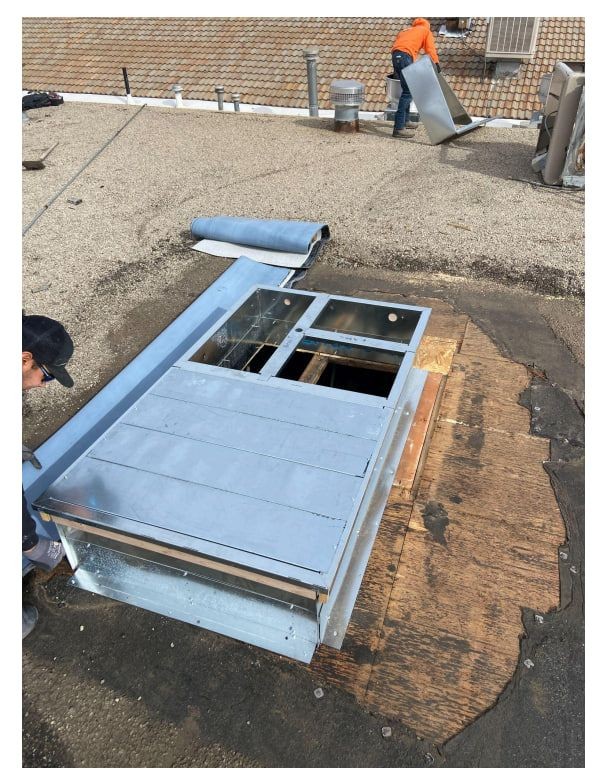 Workers installing a metal structure on a gravel rooftop with tools and materials.